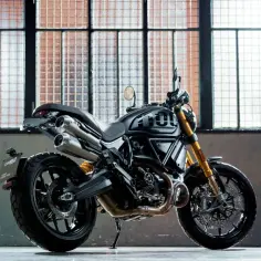 Czarny motocykl typu scrambler z podwójnym wydechem i złotym zawieszeniem. Wiele rodzajów motocykli, ten wygląda na sportowy.