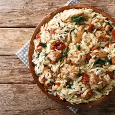 Makaron orzo z kurczakiem, suszonymi pomidorami i szpinakiem w drewnianej misce.