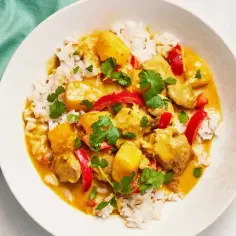 Aromatyczny kurczak curry z ryżem, papryką i kolendrą, podany w białej misce.