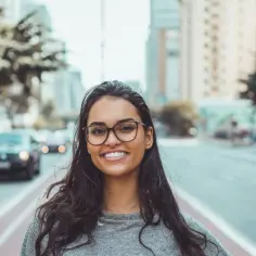 Uśmiechnięta młoda kobieta w okularach na tle miejskiej ulicy. Jej opis postaci po angielsku to "Smiling young woman with glasses on a city street.