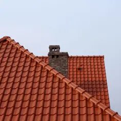 Ceglany komin na tle czerwonego, dachówkowego poddasza.