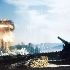 Potężna eksplozja, która wygląda jak bomba atomowa, wznosi się w niebo. Obok stoi armata, gotowa do strzału.
