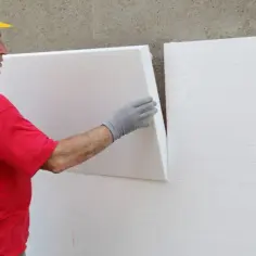 Budowlaniec w żółtym kasku montuje styropian, by obniżyć współczynnik przenikania ciepła.