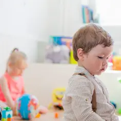 Chłopiec w żłobku, zastanawia się, czy można zapisać dziecko do żłobka w trakcie roku. W tle inne dzieci i zabawki.