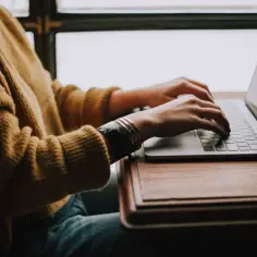Kobieta w żółtym swetrze pisze na laptopie, szukając informacji, czy pracodawca może zmusić do zmiany stanowiska pracy.