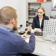 Mężczyzna przekazuje urzędniczce dokument, być może w celu uzyskania terminowego prawa jazdy.