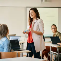 Nauczycielka wyjaśnia studentkom, jak zostać nauczycielem wczesnoszkolnym, podczas lekcji w sali komputerowej.