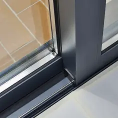 Szare, nowoczesne duże okna tarasowe z widocznym mechanizmem jezdnym i ceglaną posadzką.
