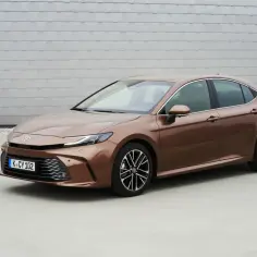 Elegancka, nowa Toyota Camry w kolorze brązowym prezentuje się stylowo na tle nowoczesnej architektury.