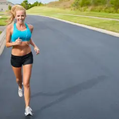 Uśmiechnięta kobieta w sportowym stroju biegnie po asfalcie, zastanawiając się, ile km biegać żeby schudnąć.