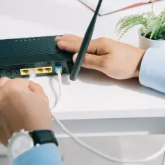 Mężczyzna podłącza kabel do czarnego rutera z dwiema antenkami.