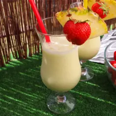 Dwa koktajle Pina Colada z ananasem i truskawkami na zielonej trawie.