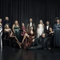 Eleganccy aktorzy Teatru Capitol Warszawa w wieczorowych strojach pozują do wspólnego zdjęcia na tle czarnej kurtyny.