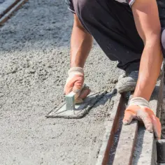 Pracownik w rękawiczkach wygładza świeży beton, dbając o właściwe proporcje i równość powierzchni.