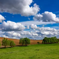 Zielone wzgórza i pola uprawne na Mazurach Garbatych pod błękitnym niebem z kłębiastymi chmurami.