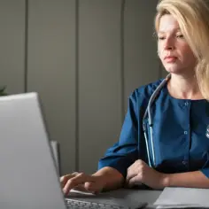 Lekarka w granatowym kitlu z fonendoskopem przy laptopie, zastanawia się, ile jest ważna recepta od psychiatry.