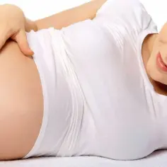 Uśmiechnięta kobieta z dłonią na brzuchu, czułe dotknięcie macicy w ciąży.