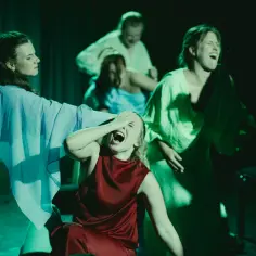 Grupa ludzi na scenie, w centrum młoda kobieta krzyczy fortissimo, zakrywając oczy.