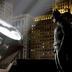 Batman stoi obok reflektora, który wyświetla jego znak na niebie nad Gotham.