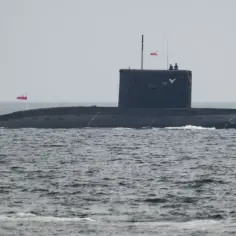 Okręt podwodny ORP Orzeł, numer burtowy 291, płynie po wzburzonym morzu. Na jego pokładzie widać dwóch marynarzy.