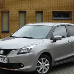 Srebrny Suzuki Baleno stoi przed żółtą ceglaną ścianą.