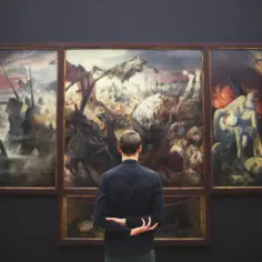 Mężczyzna wpatruje się w tryptyk przedstawiający sceny wojenne, dzieło znanych malarzy.