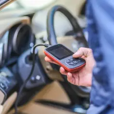 Diagnostyka Renault, być może błąd DTC B1267. Ręka trzyma skaner OBD-II przy kierownicy.