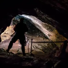 Sylwetka człowieka wchodzi do jaskini wielkiej śnieżnej, oświetlonej od środka. Skały lśnią, tworząc tajemniczy krajobraz.
