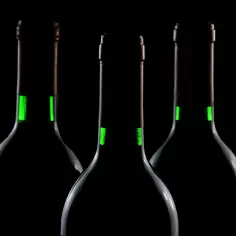Trzy butelki wina na czarnym tle. Zielone paski na szyjkach sugerują różnicę między winem wytrawnym a półwytrawnym, ile gramów cukru.