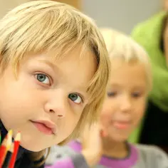 Dzieci z zespołem Aspergera, skupione na rysowaniu. W tle uśmiechnięta nauczycielka.
