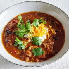 Gęste chili con carne z fasolą, mięsem i przyprawami, udekorowane śmietaną, startym serem i kolendrą. Idealne na chłodne dni.