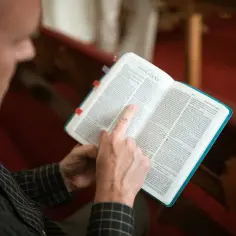 Mężczyzna czyta Biblię, wskazując palcem na tekst. Widoczny jest fragment Listu do Efezjan, część Pięcioksięgu.