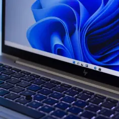 Laptop z podświetlaną klawiaturą i ekranem z niebieską tapetą Windows.