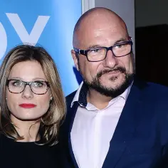 Piotr Gąsowski z żoną, uśmiechnięci, w okularach, na tle niebieskiego banera.