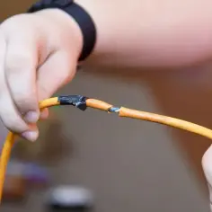 Dłonie trzymają uszkodzony przewód elektryczny, odsłaniając żyły. Różne rodzaje przewodów elektrycznych wymagają ostrożności.