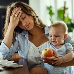 Zmęczona kobieta z dzieckiem na rękach, które płacze. Może to być obrazek symbolizujący mommy issues u kobiet, gdy życie z dzieckiem jest przytłaczające.