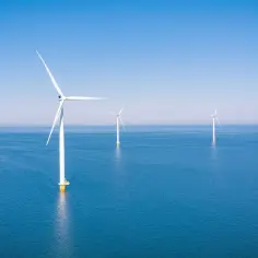 Wiatraki morskie tworzą imponujący multiplekser energii odnawialnej na spokojnym, błękitnym morzu pod bezchmurnym niebem.
