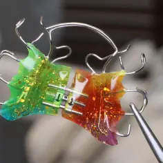 Kolorowy aparat bioblok z brokatem, zielono-czerwony, z metalowymi elementami i śrubą regulacyjną.