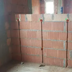 Ściana z pustaków ceramicznych z wyciętymi bruzdami pod kable. Widać trzy pionowe bruzdy z rurkami instalacyjnymi.