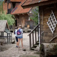 Dwie dziewczyny zwiedzają skansen, planując wykorzystać podlaski bon turystyczny 2026. W tle drewniane chaty i kurnik.