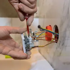 Ręce montują gniazdko, przykręcając je śrubokrętem. Widać przewody elektryczne, co pokazuje, jak podpiąć wtyczkę do kabla.