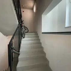 Rower na klatce schodowej to potencjalna kara za nie sprzątanie. Betonowe schody i czarne balustrady tworzą surowy widok.