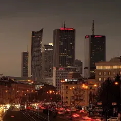 Wieczorny widok na centrum Warszawy, z nowoczesnymi wieżowcami i ruchliwą ulicą, ukazujący położenie geograficzne Warszawy.