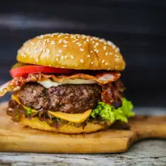 Soczysty burger z bekonem, serem, pomidorem i sałatą na desce.