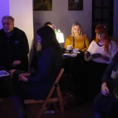 Ludzie siedzą przy stolikach, piją kawę, czytają. Może to dyskusja o tym, czym jest miłość, w kameralnej atmosferze.
