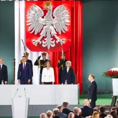 Uroczysta chwila, gdy prezydent wygłasza orędzie. Na scenie flagi Polski i UE, godło, a także osoby w mundurach.
