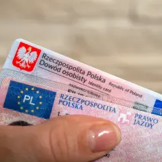 Dłoń trzyma polski dowód osobisty i prawo jazdy. Zastanawiasz się, jak odzyskać bezterminowe prawo jazdy?