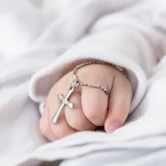 Dziecięca rączka z krzyżykiem na łańcuszku. Chrzestny na chrzciny często daje taki symboliczny prezent.