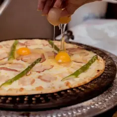 Pizza z boczkiem i szparagami, na którą wylewane jest jajko.