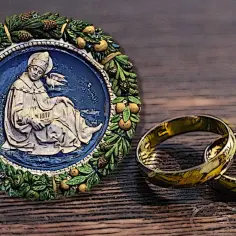 Okrągły medalion z postacią świętego i gołębiem, obok dwa złote obrączki.